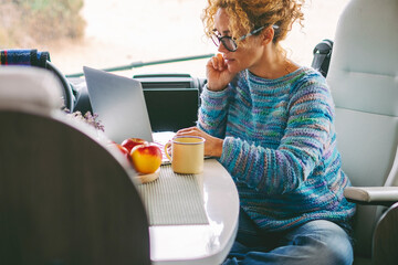 Adult nice woman work on laptop sitting in a camper van dinette enjoying freedom travel vacation or...