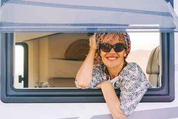 Portrait of cheerful adult woman looking outside a camper van window and enjoy travel lifestyle. Female people smile and look for a photo. Summer holiday vacation road trip tourist