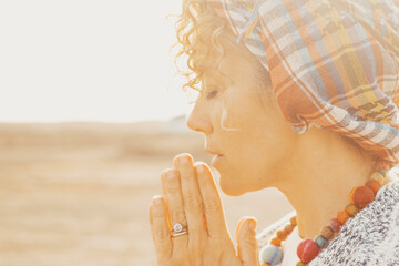 Portrait of woman with joyned hands and closed eyes pray and maditate outdoors with bright sunlight in background. Concept of meditation and inner balance life.