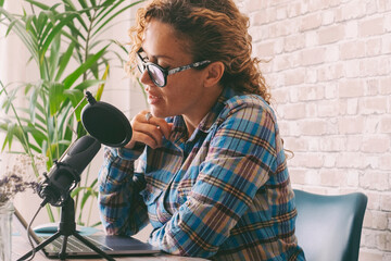 Content creator adult woman recording a podcast interview using microphone and laptop sitting at...