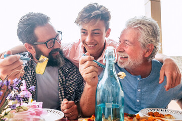 Father grandfather and son eaing together having fun. father's day concept celebration with men family enjoying meal on the table. Cheerful man young adult and mature laughing and having lunch - obrazy, fototapety, plakaty