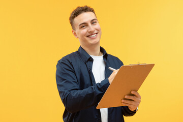 Positive young guy taking notes in clipboard and smiling