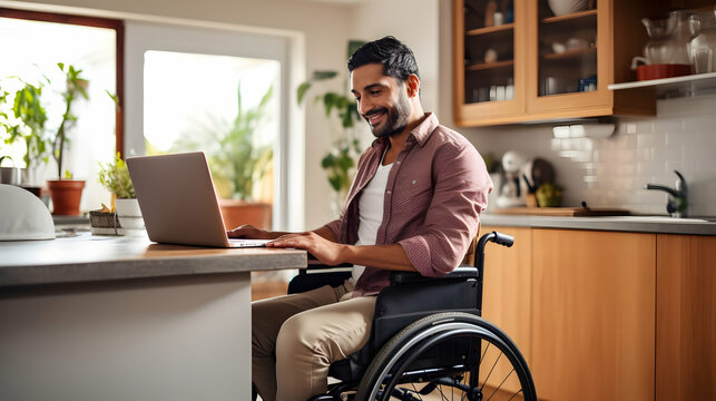 Joyful indian man in wheelchair holding laptop on knees while staying in middle of bright open-plan kitchen,Generated Ai