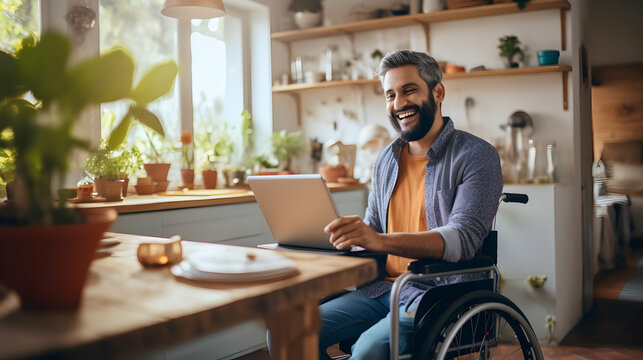 Joyful indian man in wheelchair holding laptop on knees while staying in middle of bright open-plan kitchen,Generated Ai