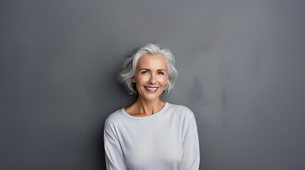 Close up portrait of beautiful older woman smiling and standing by grey wall.