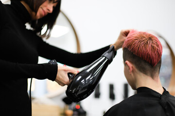 The hairdresser dries the woman's freshly dyed pink hair with the hairdryer.
