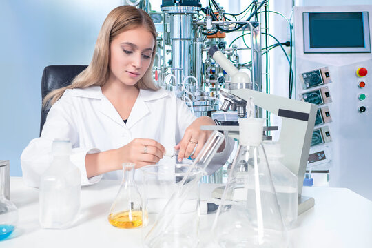 Woman laboratory assistant. Girl at table with bottles. Bioreactor near scientist. Biologist woman works with microscope. Using bioreactor for scientific experiments. Scientist uses bioreactor