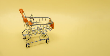 Small cart on a yellow background. Small supermarket grocery push cart for shopping. Shopaholic....