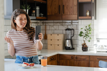 Young woman influencer vlogging over her smartphone in her modern home kitchen