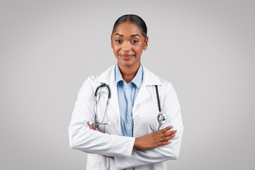 Smiling confident friendly millennial black lady doctor in white coat, with stethoscope, crossed arms