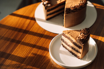 Cut puff chocolate piece from a cake on a white plate on a wooden table.