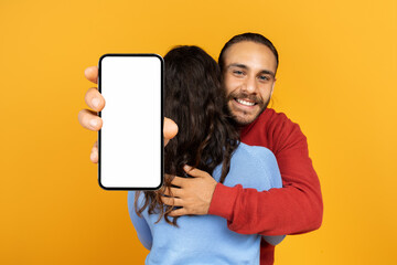 Millennial man hugging his girlfriend holding huge phone in hands