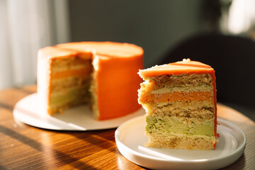 A piece of pistachio cut from a cake on a white plate on a wooden table under the morning sunlight.