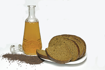 A decanter with natural yellow mustard oil, black mustard seeds sprinkled next to it and gray bread...