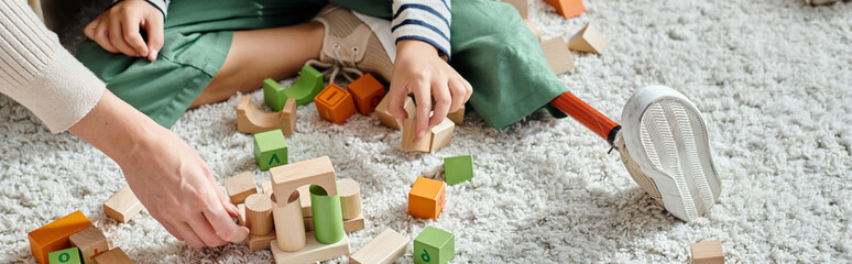 cropped banner, girl with prosthetic leg sitting on carpet and playing with wooden toys near mother