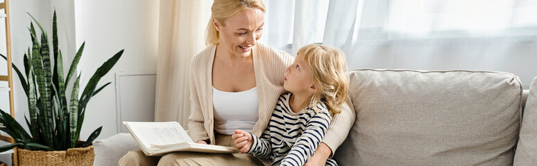 happy mother reading book to blonde daughter while sitting together in modern living room, banner - Powered by Adobe