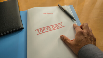 Hand of a man opening a folder with top secret documents. Confidential documents on the desk. 