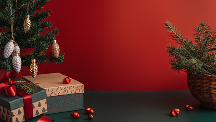Table with gift and Christmas trees in decorations in front of red background.