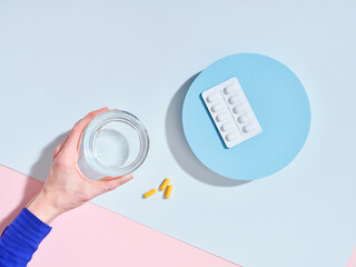 Flat lay creative composition with food supplement pills, glass of water and female hand on colorful background