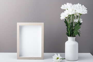 Empty photo frame and bouquet of white chrysanthemums, daisies in a white vase.Greeting card, home interior.