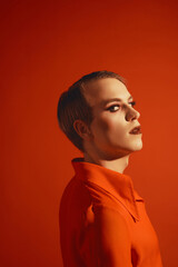 Portrait of young guy in bright jacket, makeup with colorful eyes and lashes posing against red studio background. Concept of male makeup, fashion, lgbtq community, self-identity, acceptance