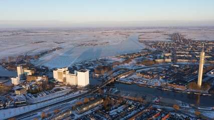 Aerial shot of a city, with a frozen river and snowy fields on a cloudy winter day