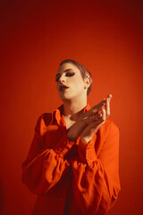 Portrait of young transgender man in colorful jacket and bright makeup with lash extensions posing against red studio background. Concept of male makeup, fashion, lgbtq community, self-identity