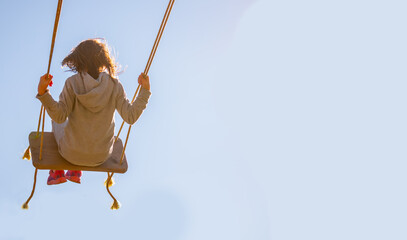 Young girl flying on swing against blue sky. Happy childhood, freedom concept. Copy space.