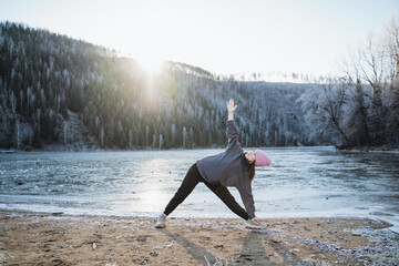 Asana inverted triangle, girl practicing yoga in winter on the shore of a frozen lake, meditation in nature, morning sunlight.