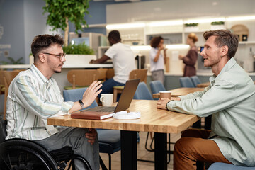 Young businessman with disability discussing online presentation on laptop together with his colleague at meeting