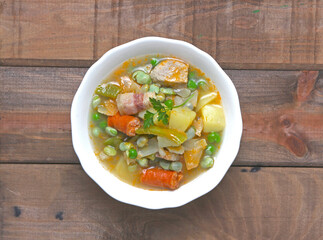 Broad bean soup, with vegetables, potatoes, meat, bacon and chorizo, on a white plate, photographed on dark wood.