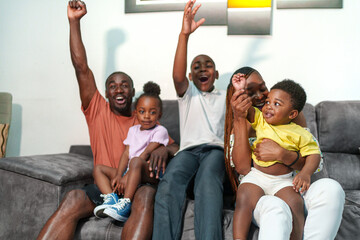 Joyful African family enjoys football match on TV, celebrating a goal together in living room.