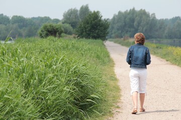 Back view of an old woman walking on the road near with grasses on the side