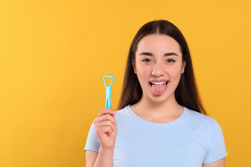 Happy woman with tongue cleaner on yellow background, space for text