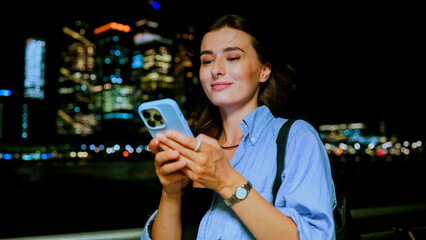 Pretty happy cute young Caucasian woman looking at phone and typing messages with smile. Attractive...