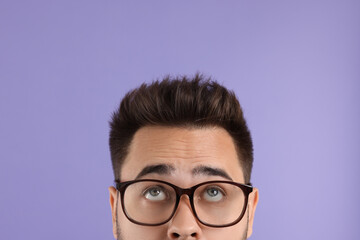Man in glasses looking up on violet background, closeup