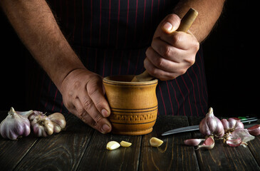Close-up of a man's hands crushing garlic with a wooden pestle and mortar. We are preparing a...