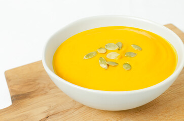 Pumpkin cream soup with seeds in a gray bowl on a wooden cutting board. Concept of healthy eating. Vegetarian and vegan food. Horizontal orientation.
