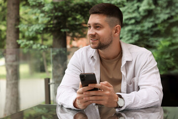 Obraz na płótnie Canvas Handsome man sending message via smartphone at table in outdoor cafe