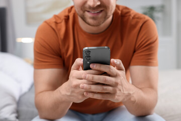 Man sending message via smartphone on bed at home, closeup