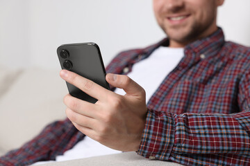 Man sending message via smartphone on sofa indoors, closeup