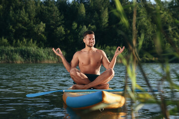 Man meditating on color SUP board on river