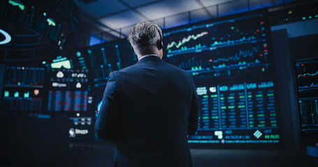 Back View of a Middle Aged Stock Exchange Trader Following a Live Auction, Communicating Buy and...