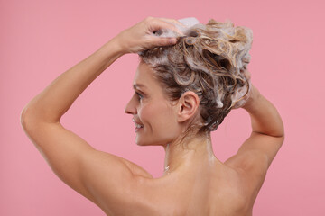 Beautiful happy woman washing hair on pink background