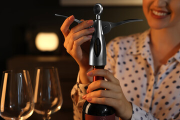 Romantic dinner. Woman opening wine bottle with corkscrew indoors, closeup