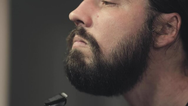 Brutal bearded man shaves his beard, morning tradition, self-care at the mirror. Barbershop and cosmetology. Close-up portrait, facial features and handsome man. Shaving machine