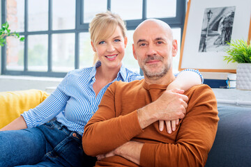 Blond haired woman and mid aged man sitting on sofa at home and relaxing together