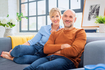 Blond haired woman and mid aged man sitting on sofa at home and relaxing together