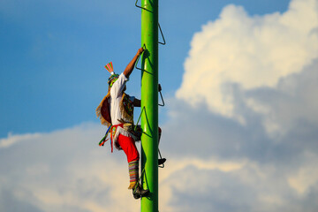 isolated papantla flyer climbing a very tall metal pole without basic safety gear, getting ready to...