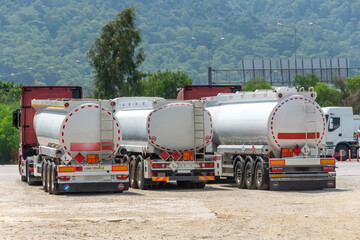 Parking row jam of trucks with fuel tanks in front of a warehouse and storage of huge tanks of raw material containers, next to the main highway